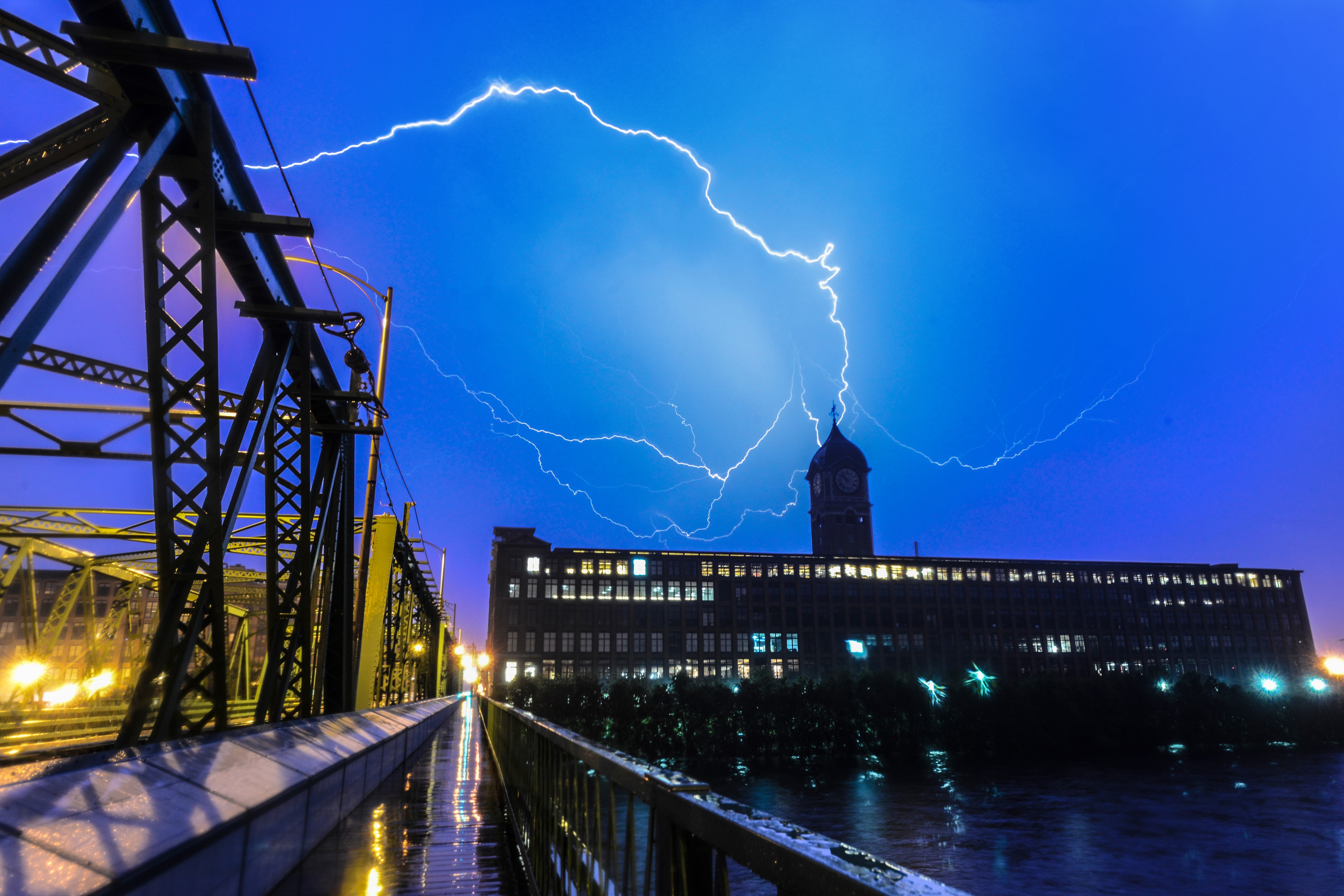 Lightning strikes over a mill building and clock tower at night, photographed by Scott Proposki