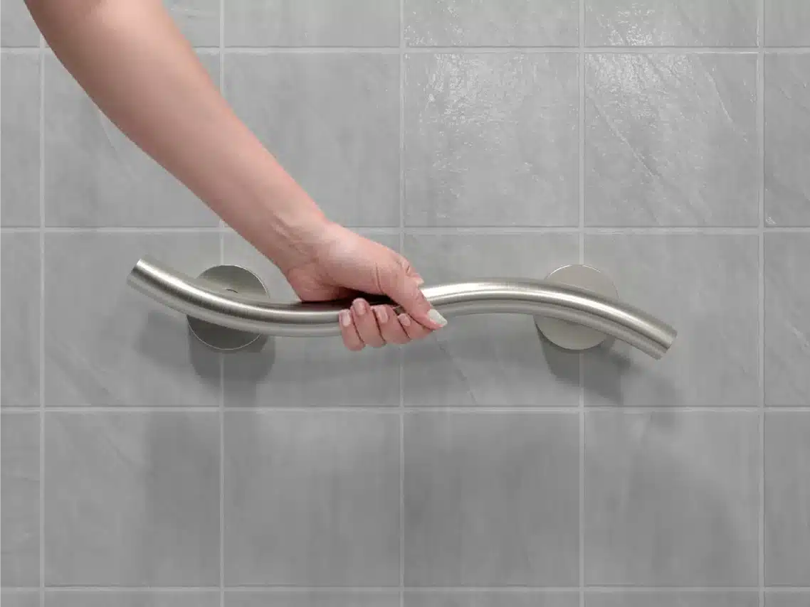 Hand gripping the curved bi-level rail of a WAVE grab bar in a residential bathroom