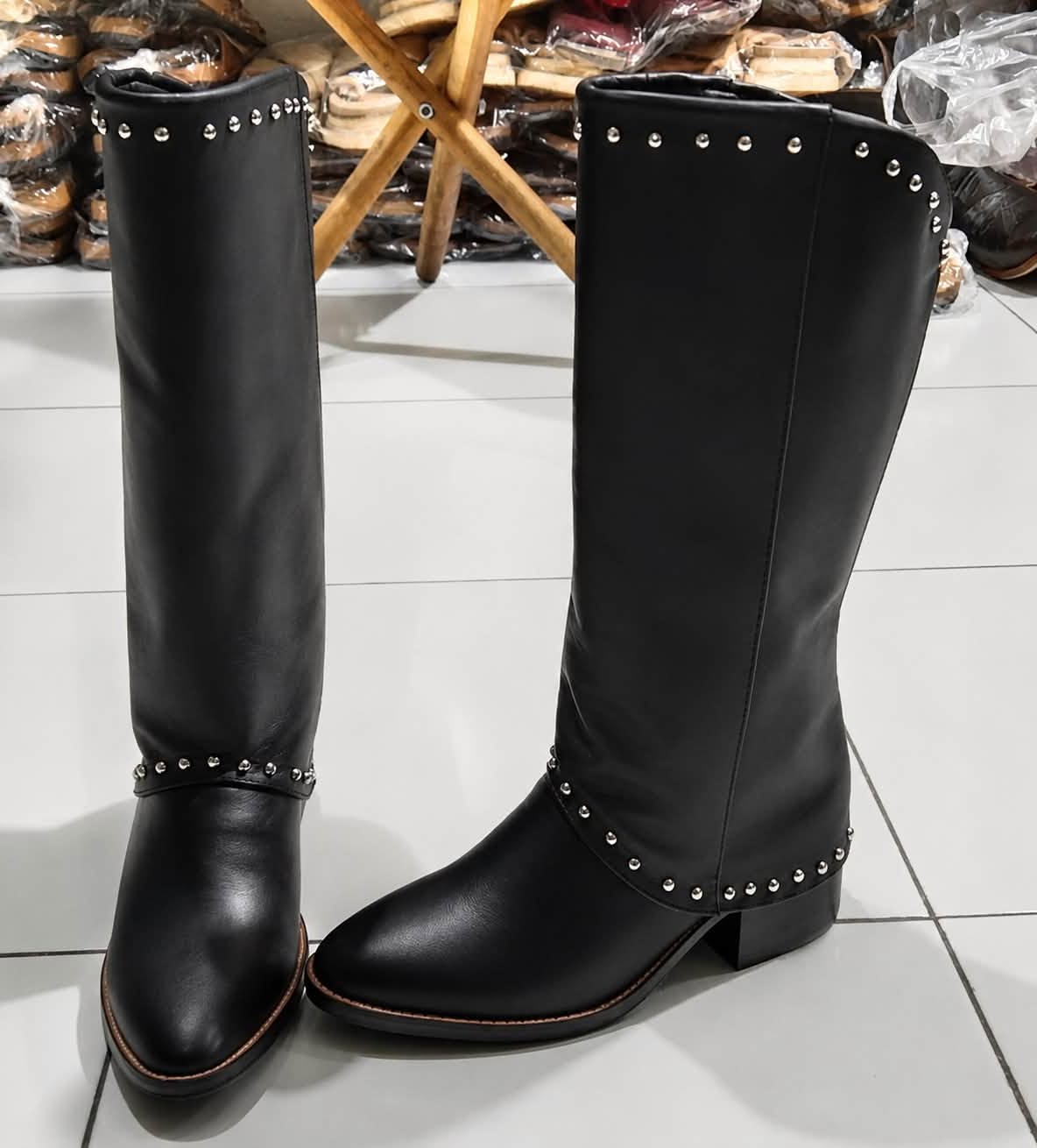 Black leather knee-high boots with silver stud detailing on boutique floor