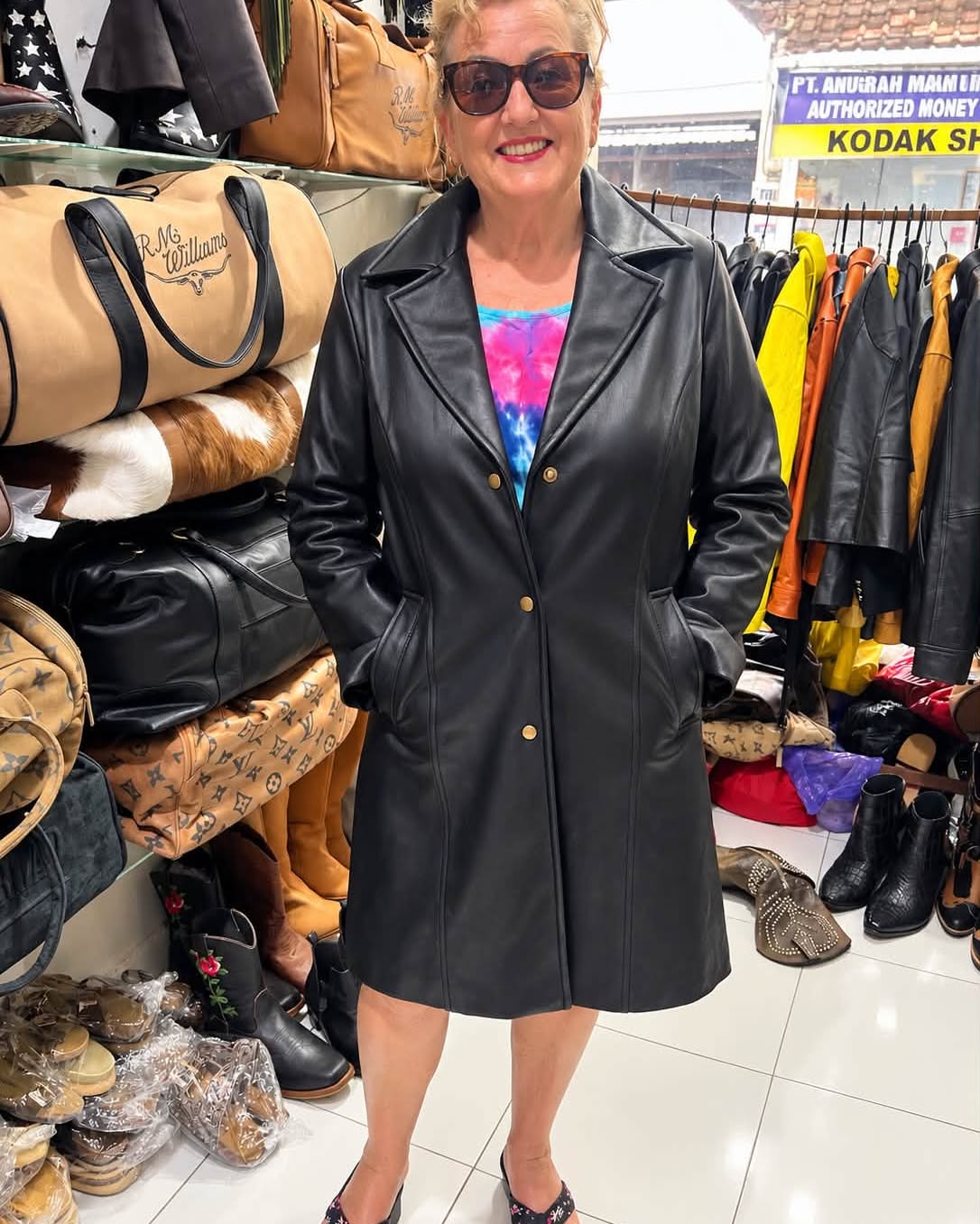 Woman wearing a long black tailored leather coat with gold-tone buttons